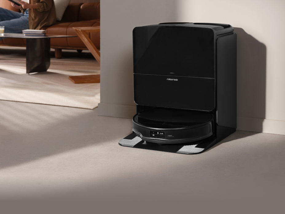 White Roborock Qrevo Curv 2 Flow robot vacuum docked in a curved white base station against a green paneled wall